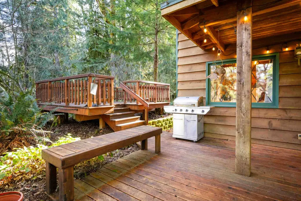 A cozy, relaxed wooden deck with a grill, surrounded by greenery and equipped with a comfortable bench. The deck offers opportunities for sunset barbecues, stargazing, and enjoying morning coffee outdoors.