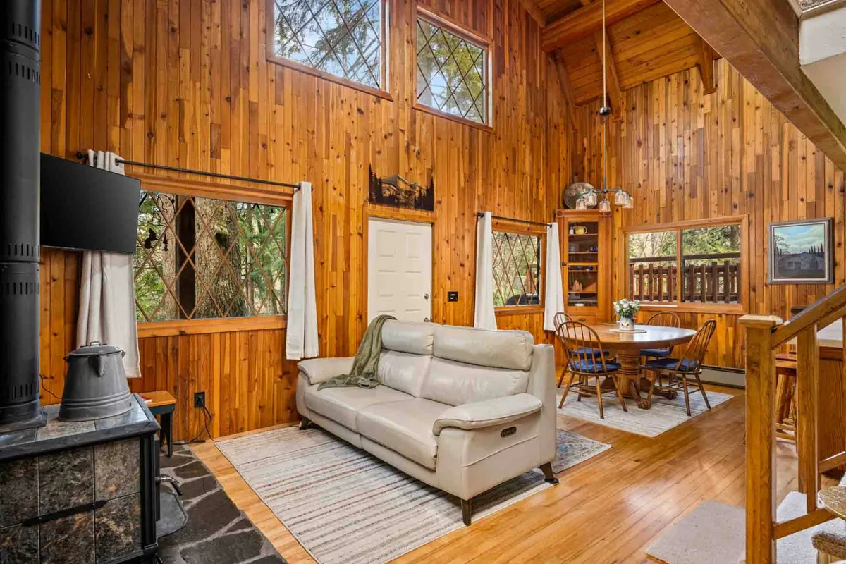 A welcoming open-concept area featuring wooden wall paneling, a leather sofa, dining table, and a wooden staircase. The space exudes warmth, with sunlight streaming in and the inviting ambiance ideal for family games or quiet relaxation.