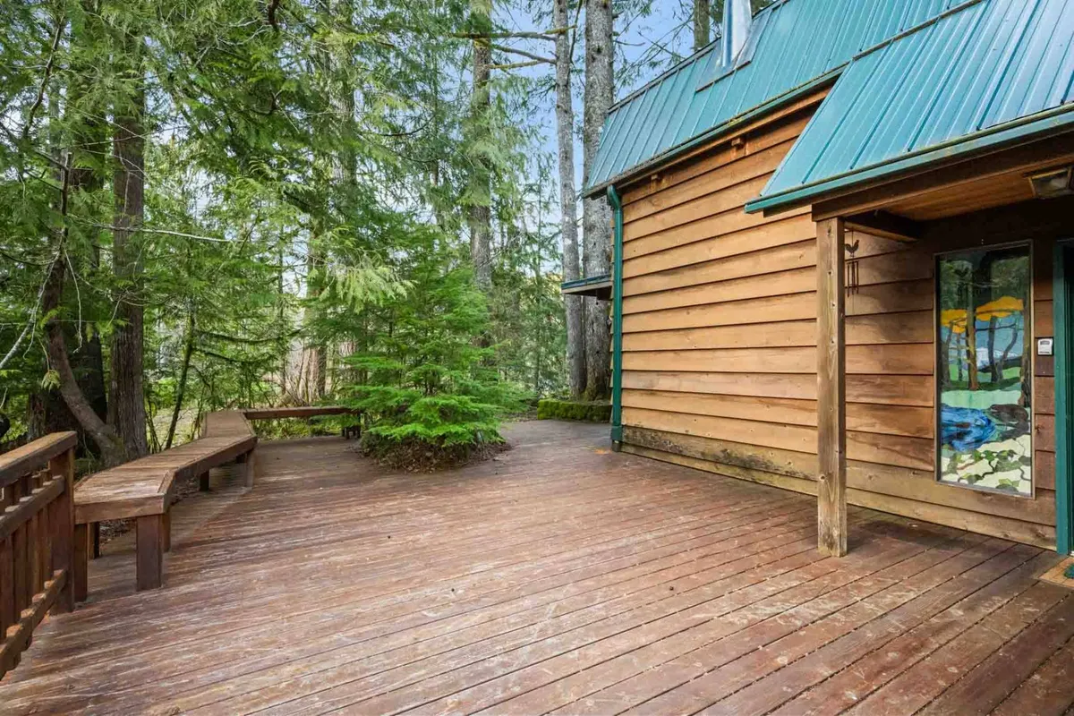 A peaceful wooden deck framed by forest, adjacent to a unique stained glass window, blending rustic charm with artistic detail. The secluded setting evokes a sense of quiet and privacy, ideal for board games or contemplative moments.