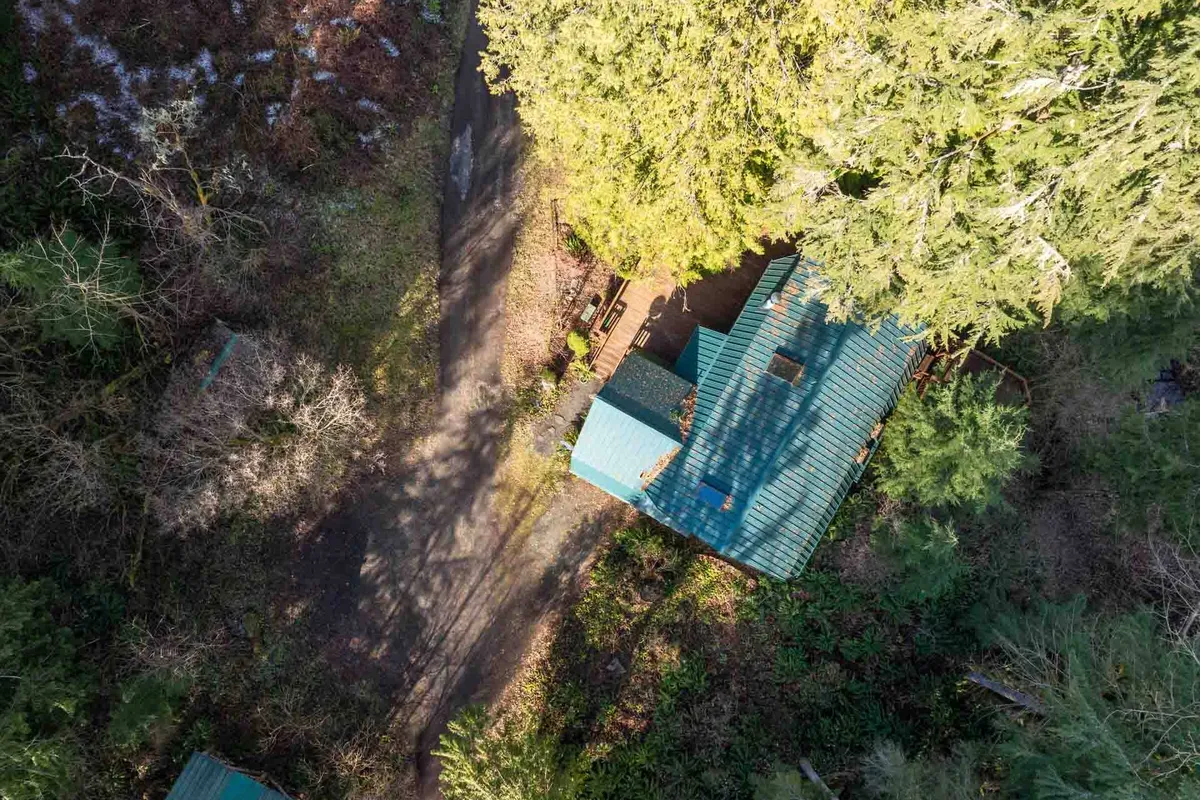 A rustic cabin nestled among tall trees, with a winding path leading up to the porch. The warm glow of sunset bathes the porch, inviting guests to relax and enjoy the natural tranquility surrounding the home.